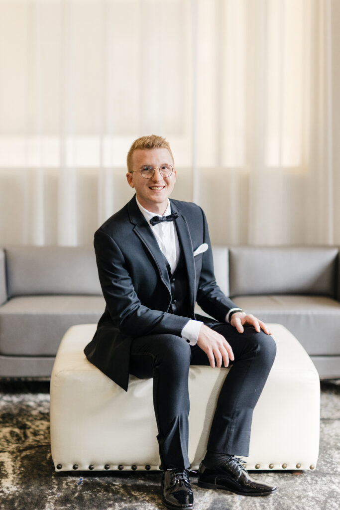 Candid moment of the groom smiling as he prepares his bow tie at Embassy Suites Pittsburgh.