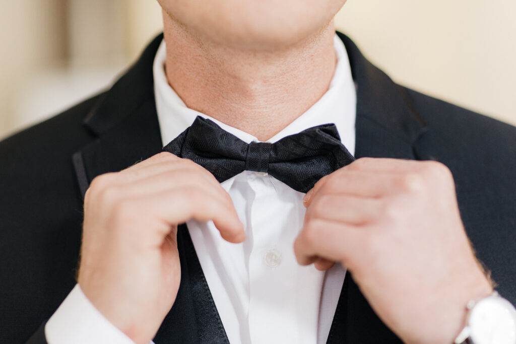 Groom adjusting his bow tie while sitting and smiling at Embassy Suites Pittsburgh Downtown