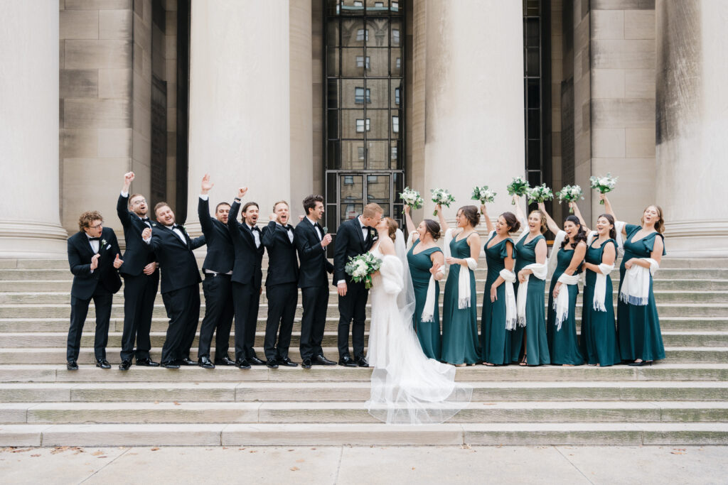 Bridesmaids and groomsmen cheering enthusiastically as the bride and groom share a kiss at Embassy Suites Pittsburgh Downtown