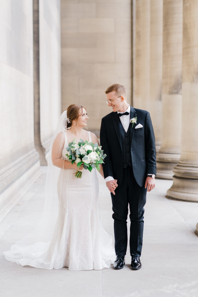 Bride and groom holding hands while walking together at Mellon Institute Columns.