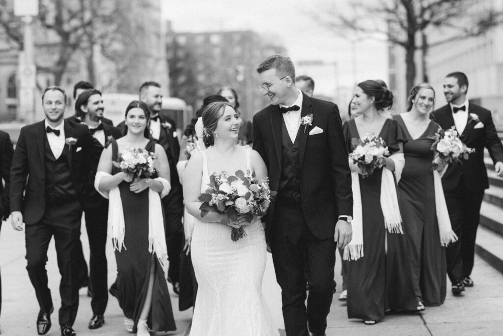 Full bridal party walking in front of the Mellon Institute Columns in a timeless black-and-white capture.