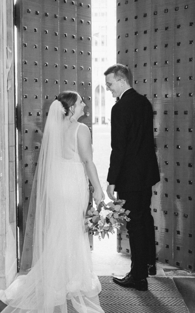 Couple opening the grand doors of Heinz Chapel in a dramatic black-and-white moment.